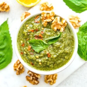 A bowl of vegan walnut pesto topped with fresh basil leaves and walnuts.