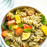 a bowl of veggie pesto pasta topped with fresh basil