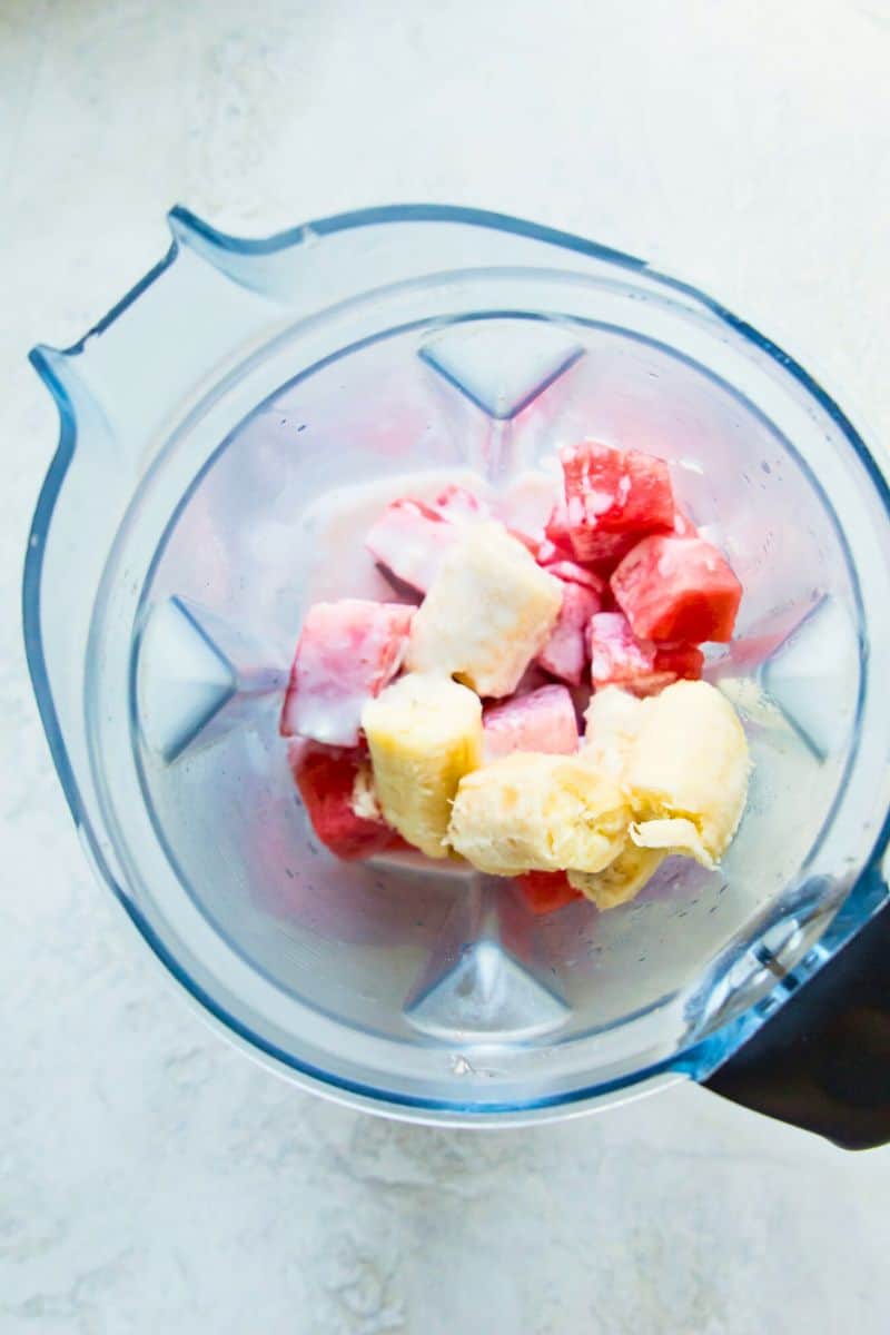 A blender with chopped banana and watermelon in it.