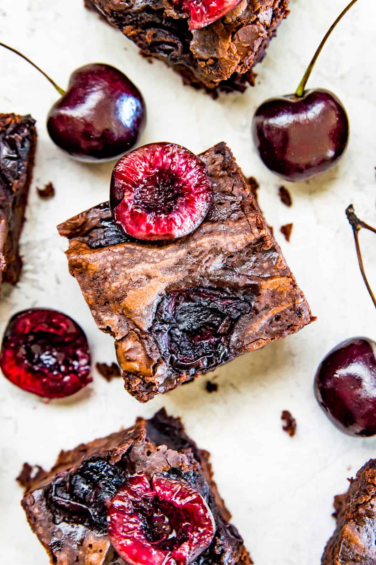 Cut up cherry brownies with fresh cherries on top surrounded by fresh cherries.