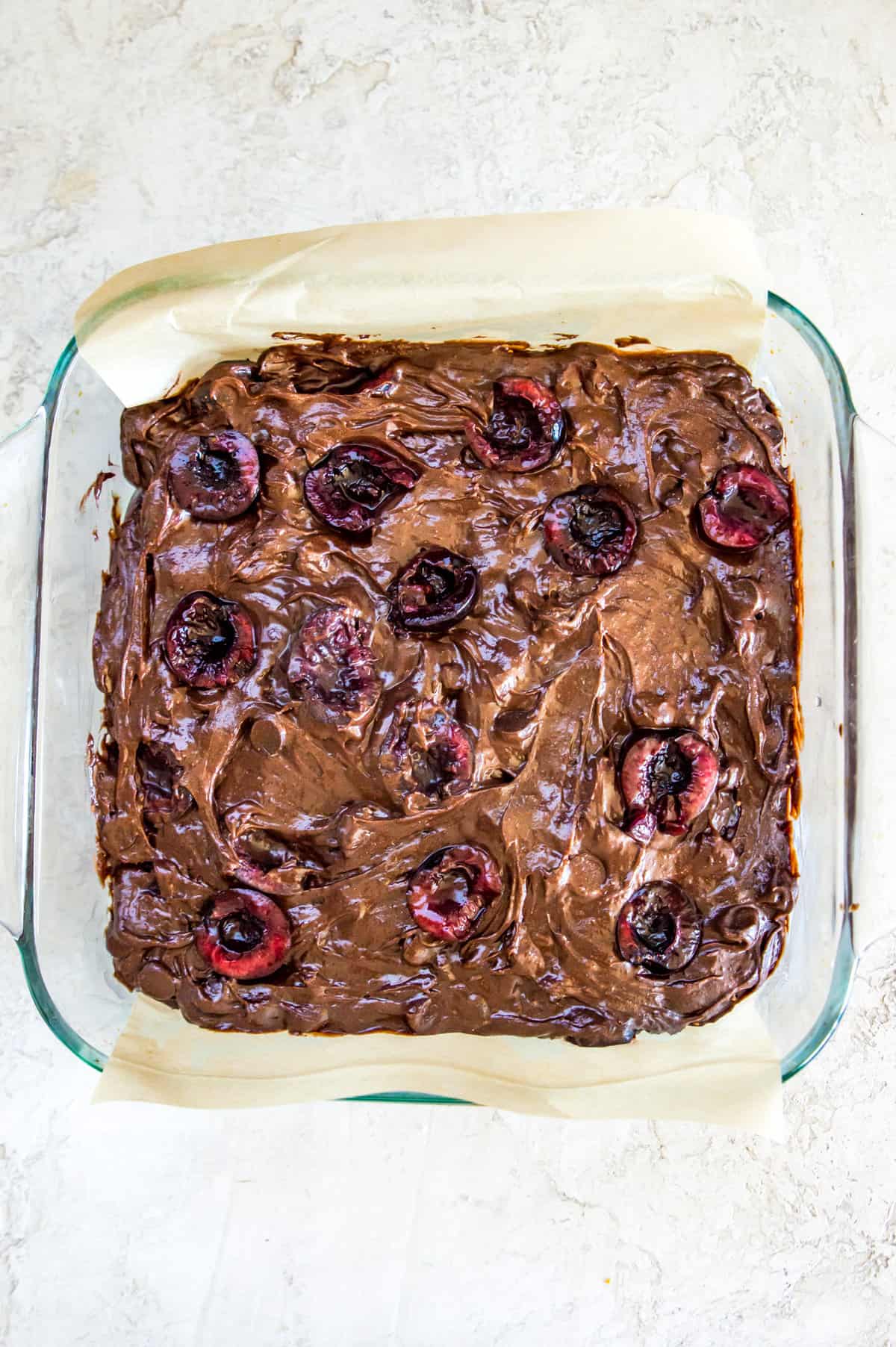 A glass baking pan with a brownie batter topped with chopped cherries in it.