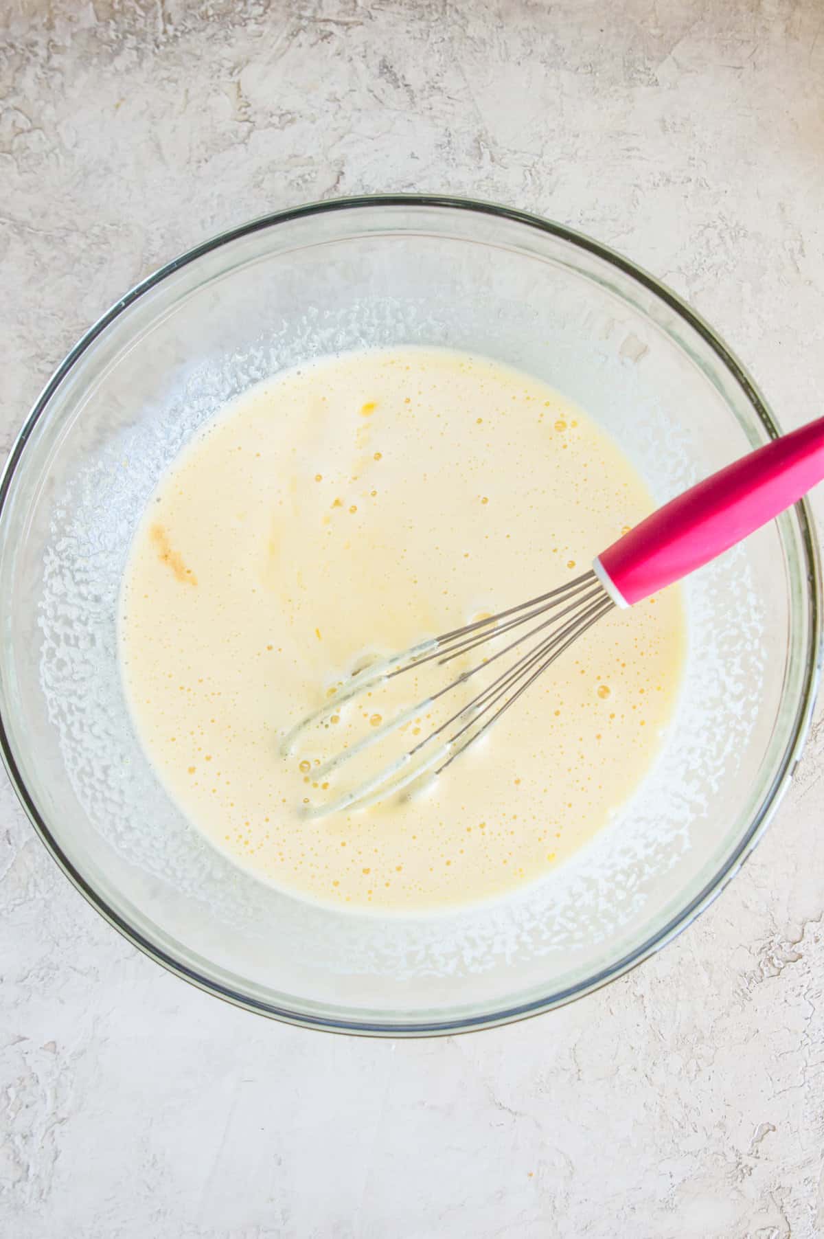A glass bowl with a frothy liquid in it with a whisk in the liquid.
