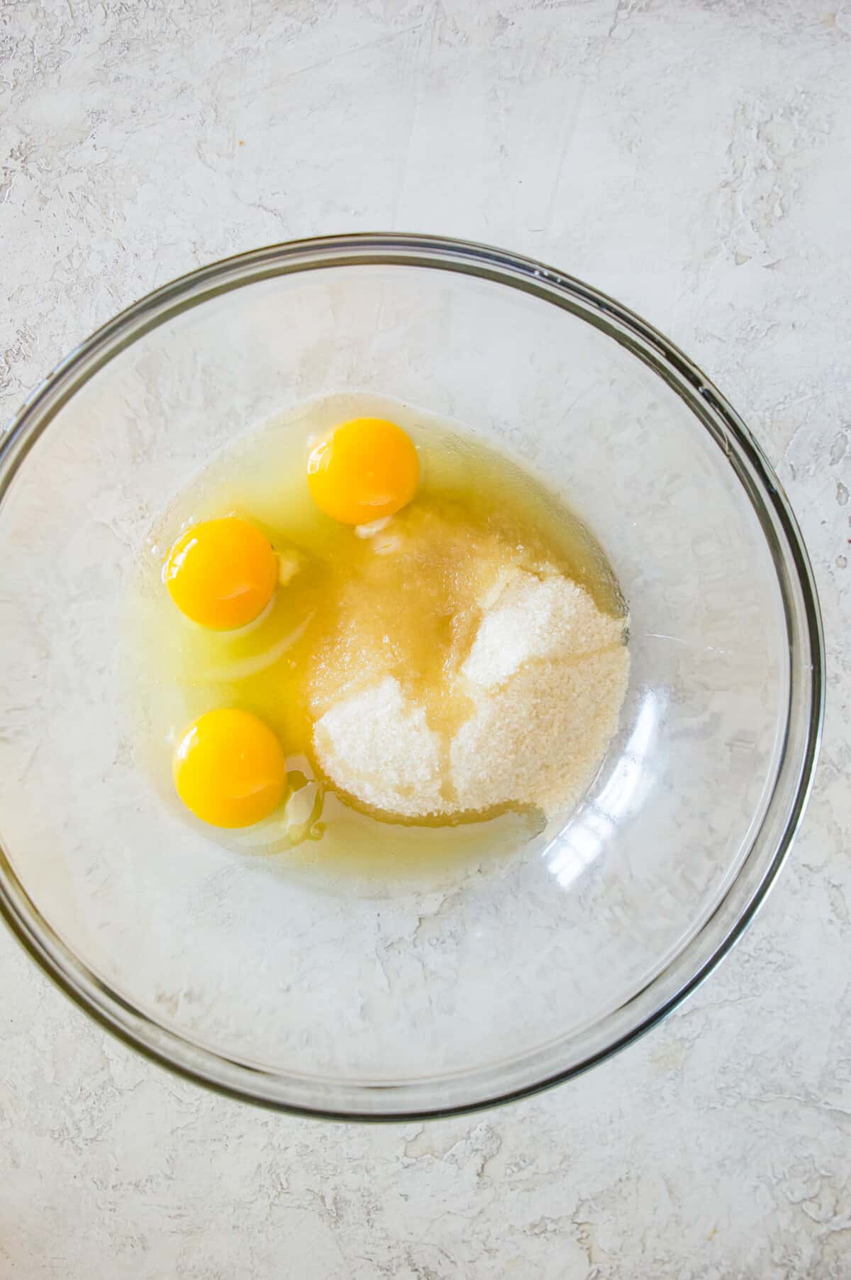 A glass bowl with eggs and sugar in it.
