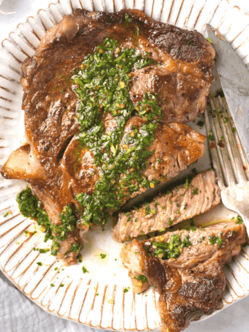 A plate with a cut up steak on it covered in chimichurri sauce.