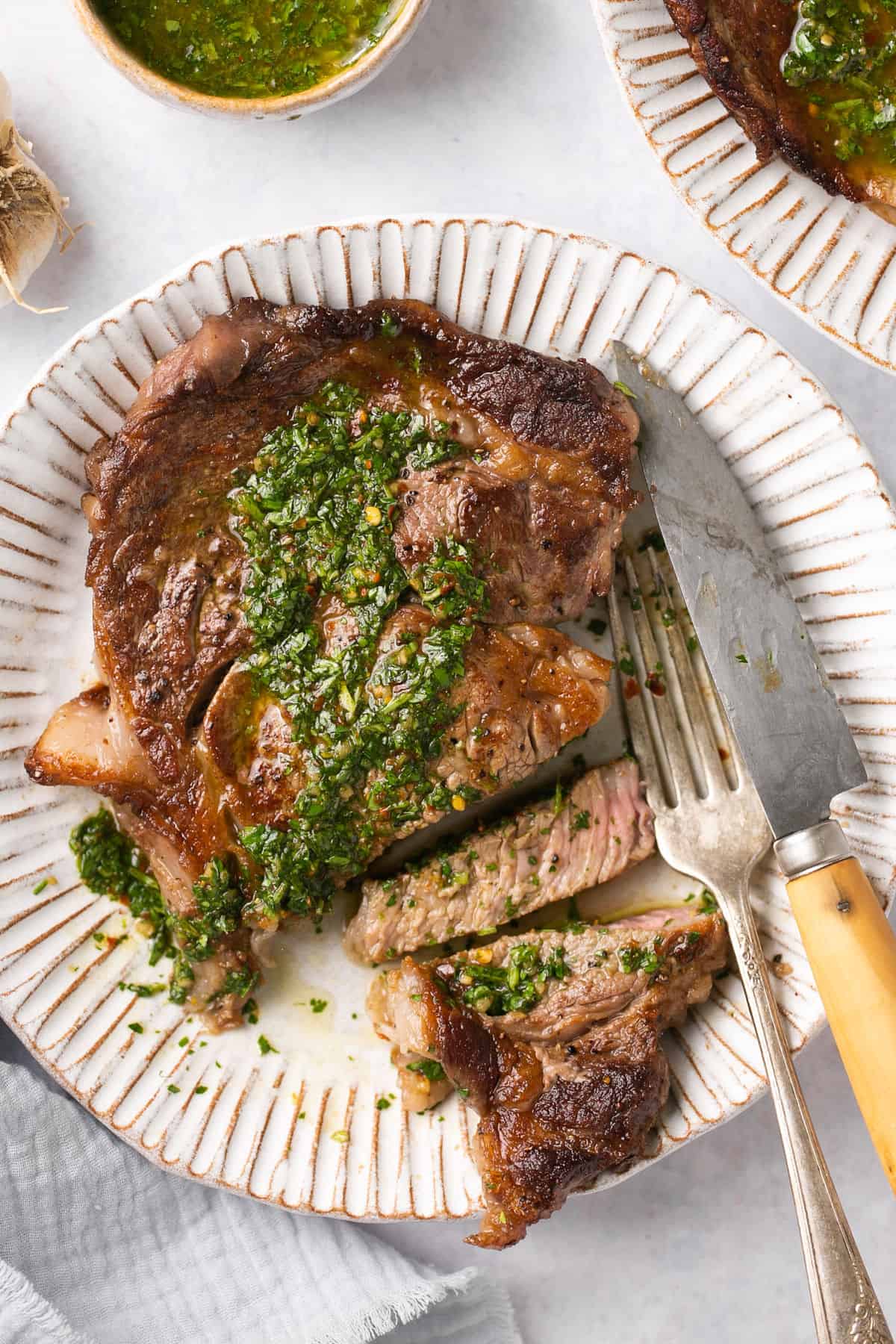 A piece of Denver steak with chimichurri on it on a white plate with a fork beside it.