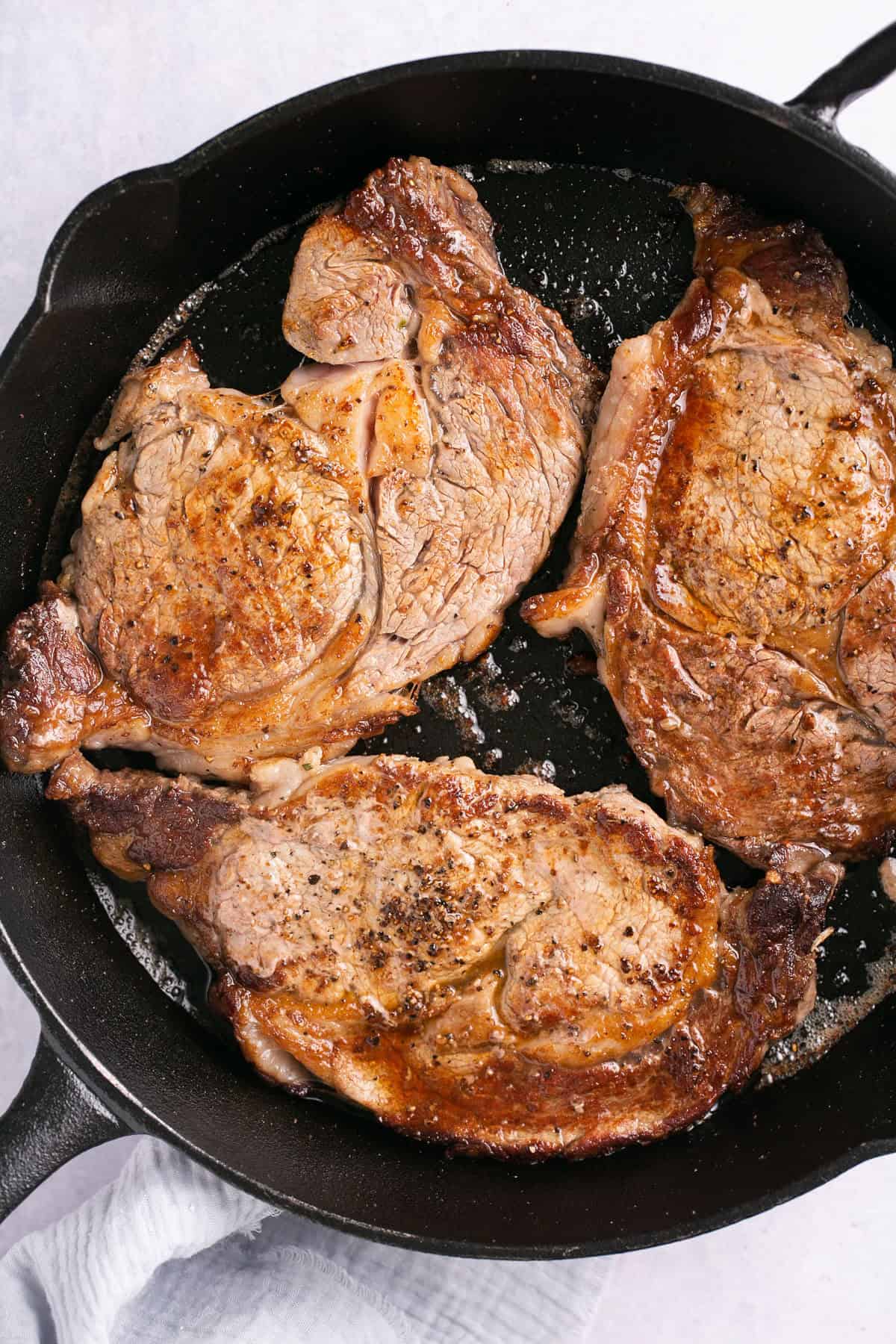 Three steaks cooking in a cast iron skillet.