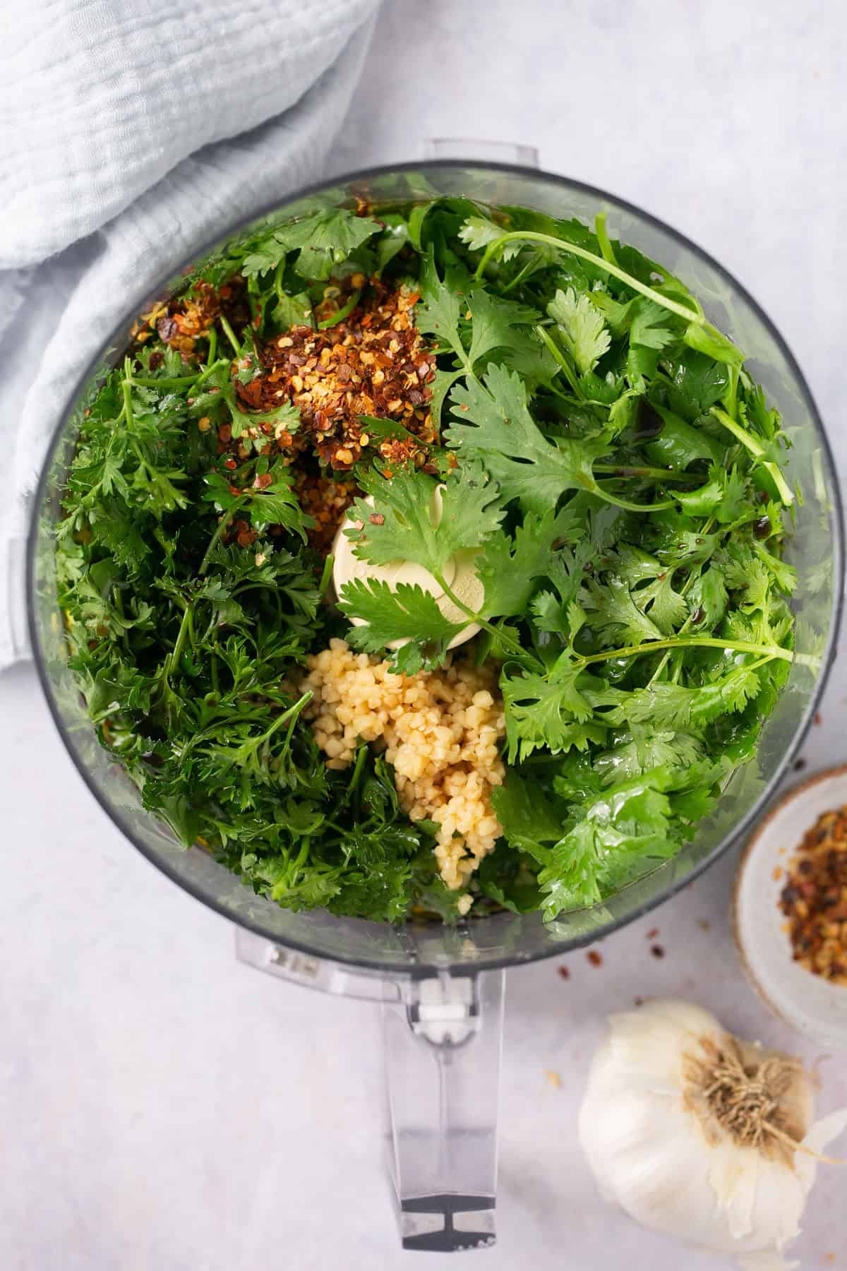 A food processor with fresh herbs and garlic in it.