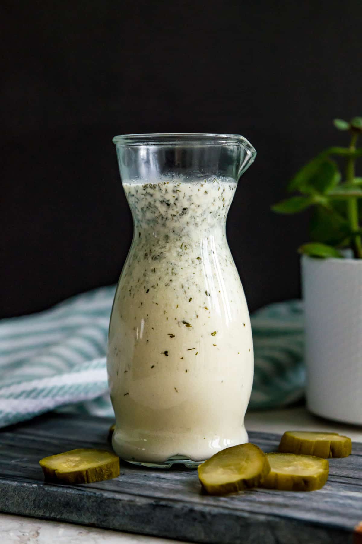 A jar of dill pickle salad dressing on a cutting board with chopped pickles around it.