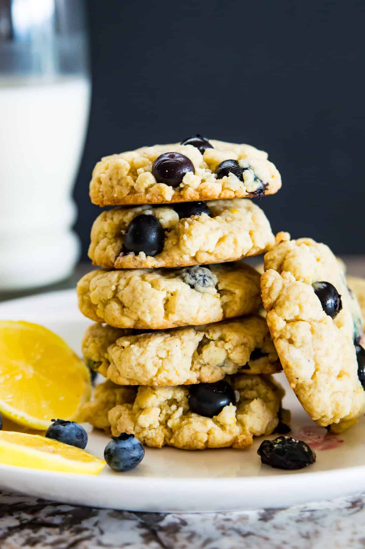 A stack of lemon blueberry cookies on a plate with a glass of milk behind it.