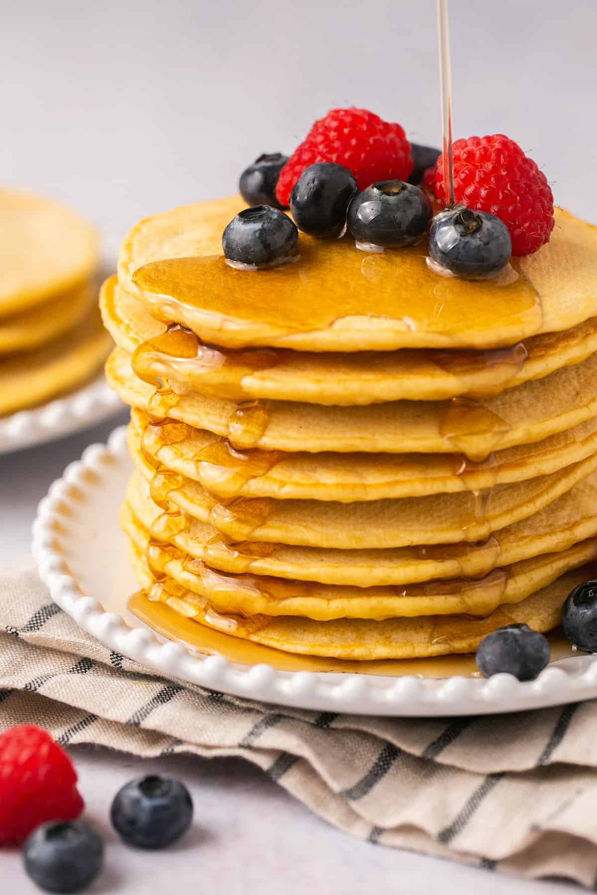 A stack of oat milk pancakes with berries on top and syrup being poured on it.