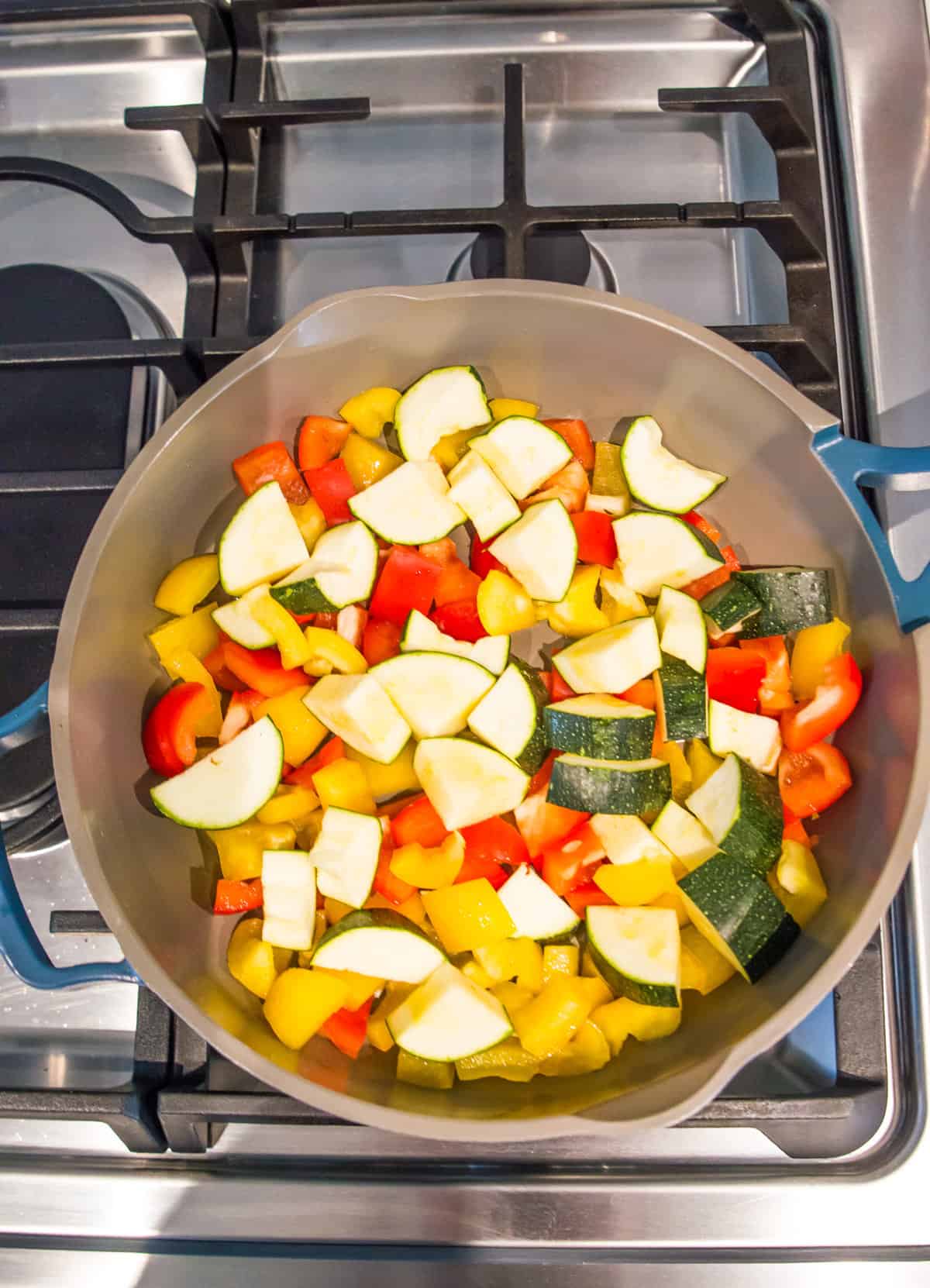 Chopped zucchini and bell peppers cooking in a pan on a stovetop.