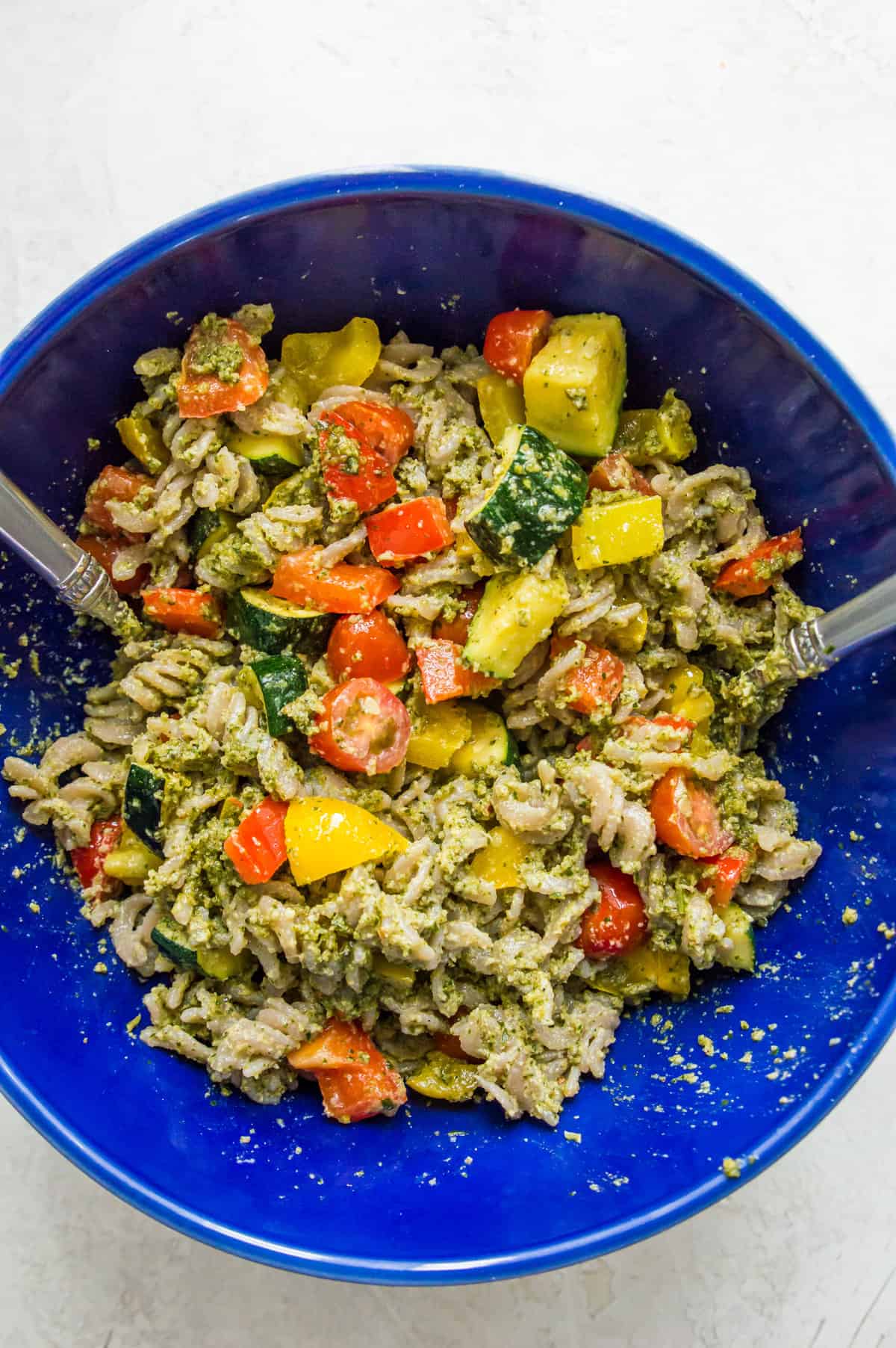 A bowl with chopped vegetables in it and cooked pasta topped with pesto sauce.