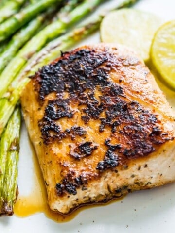 A piece of blackened mahi mahi on a plate with cooked asparagus and lime wedges beside it.