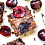 A cherry brownie topped with a fresh cherry cut in half.