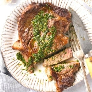 A plate with a cut up steak on it covered in chimichurri sauce.
