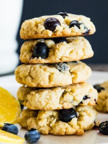 A stack of five lemon blueberry cookies on a plate with lemon slices.