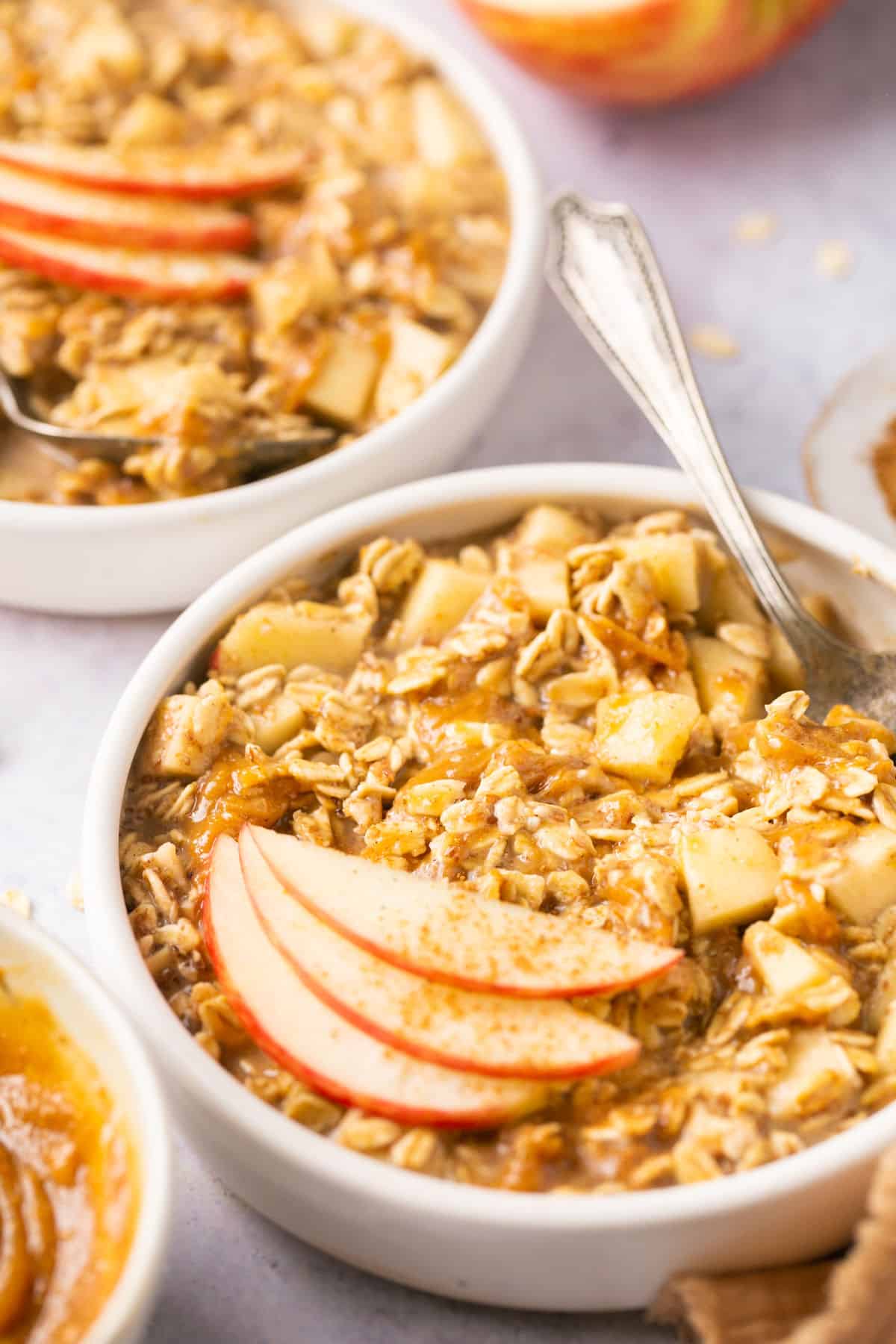 A bowl of apple pie overnight oats topped with apple slices and with a spoon in it.