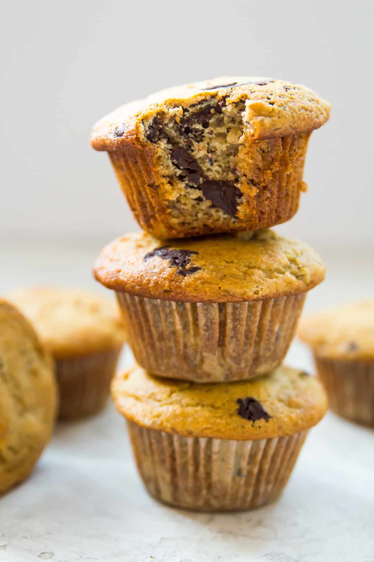 A stack of three banana muffins with chocolate with a bite out of the top muffin.