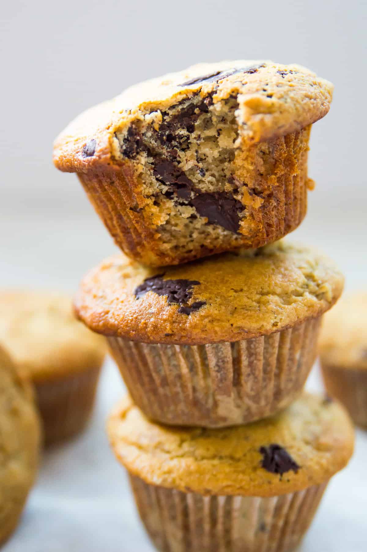 A stack of three banana chocolate muffins and the top muffin has a bite out of it.