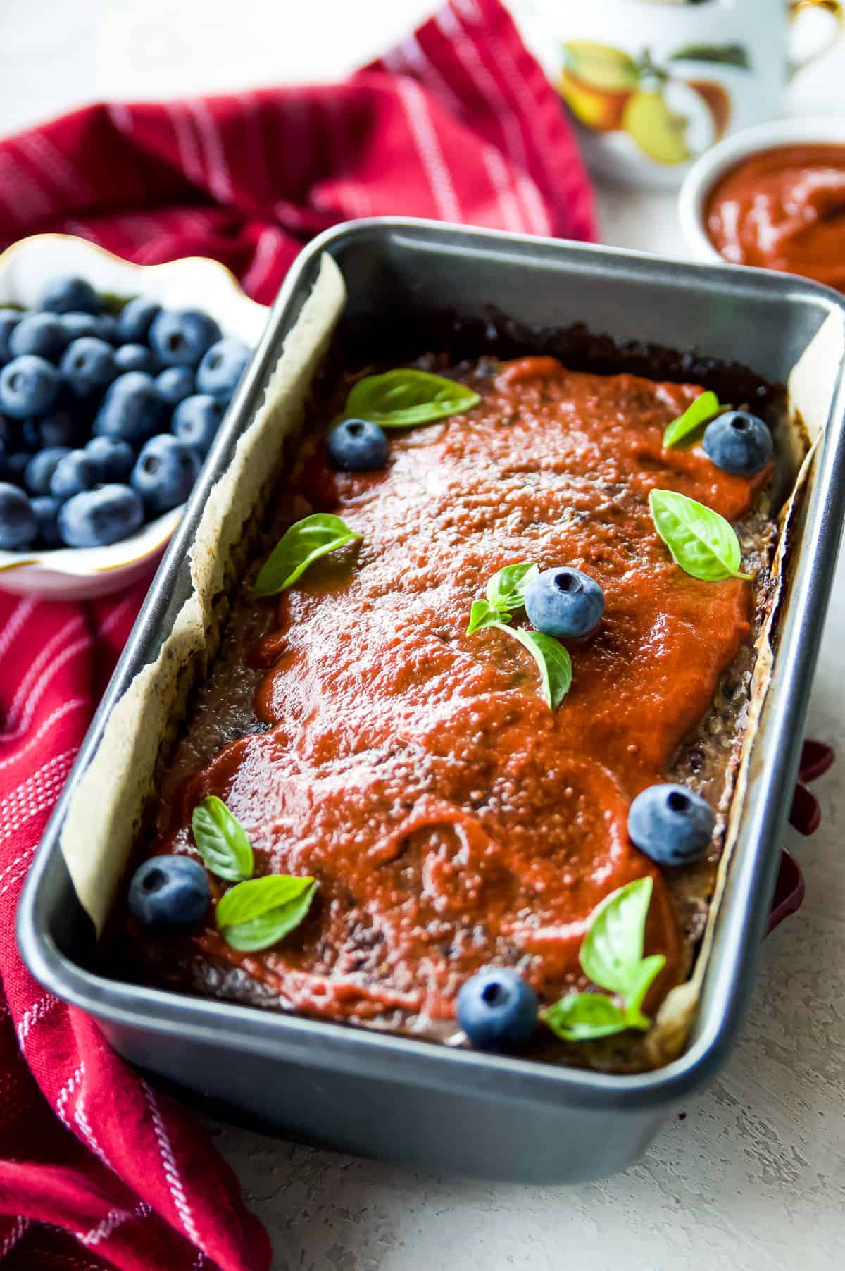 Meatloaf in a pan topped with bbq sauce, fresh blueberries and basil leaves.