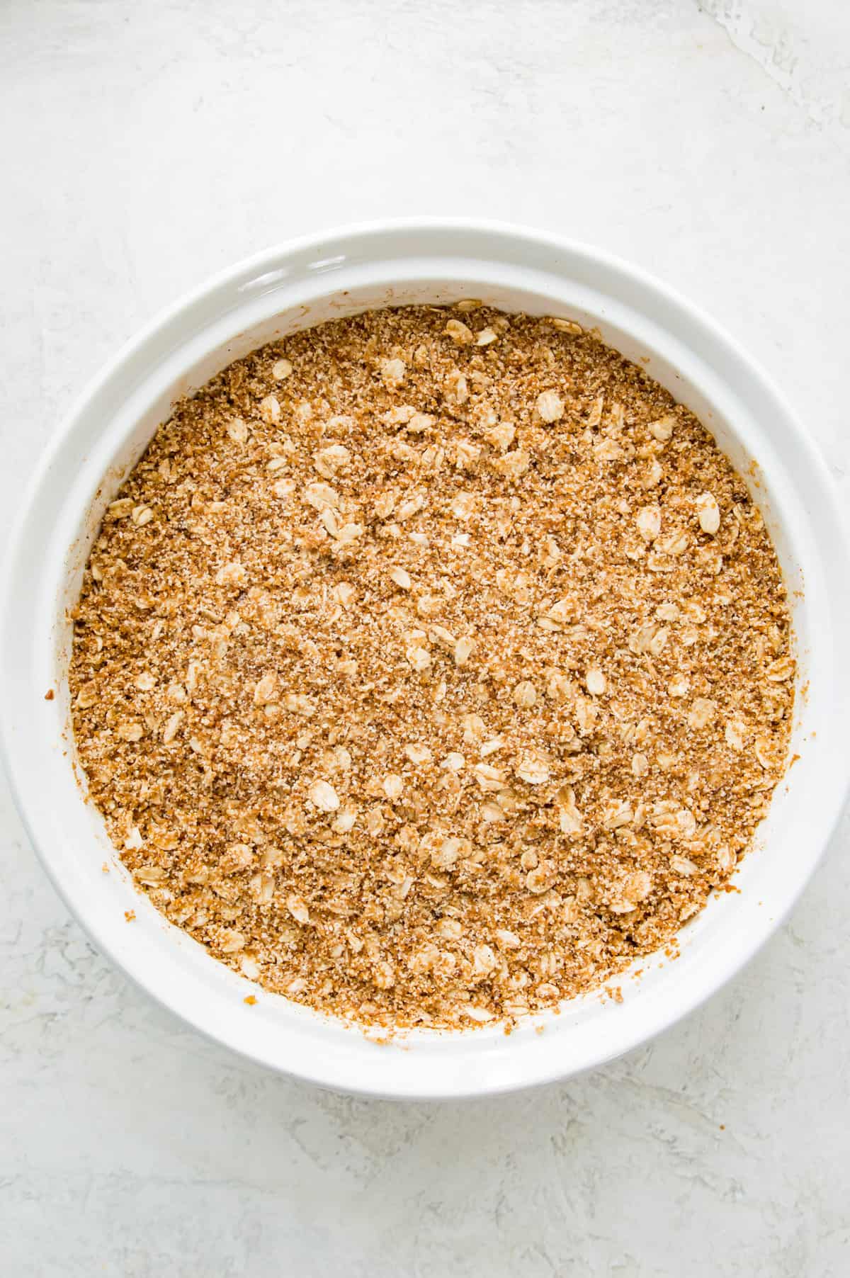 An unbaked apple crumble in a white casserole dish.