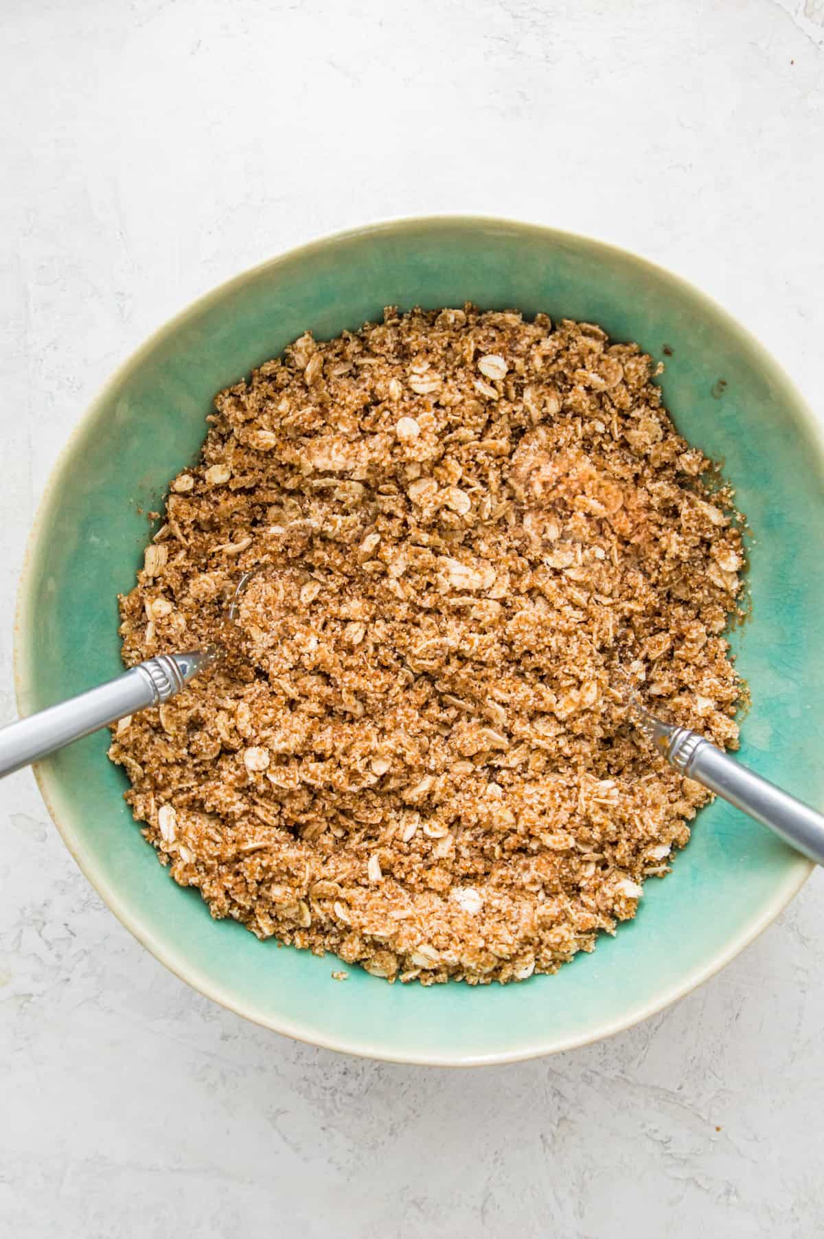 A bowl filled with an oatmeal and sugar mixture with two spoons in it.