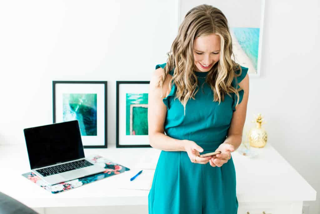 Erin Carter using her cellphone with a desk and a laptop behind her.