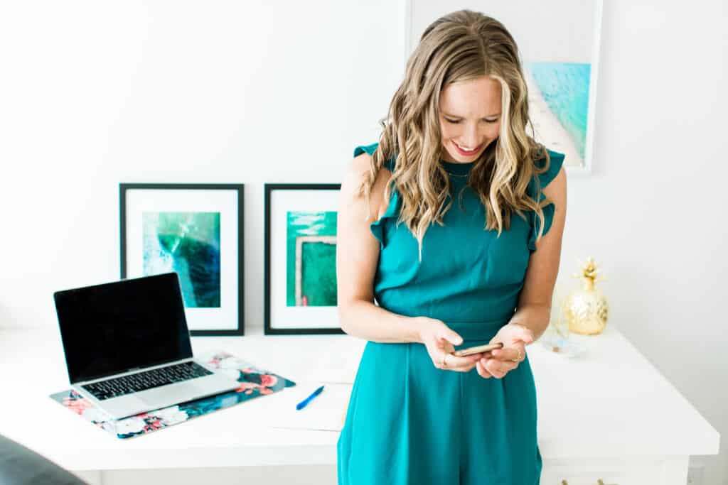 Erin Carter using her cellphone with a desk and a laptop behind her. 