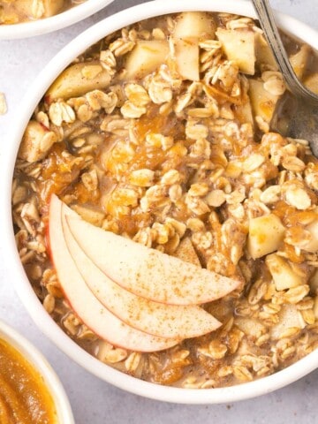 A bowl of apple pie overnight oats topped with apple slices and with a spoon in it.