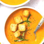 Bowls of butternut squash and red pepper soup topped with croutons.