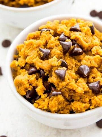 A bowl of edible pumpkin cookie dough with chocolate chips with a spoon in it.