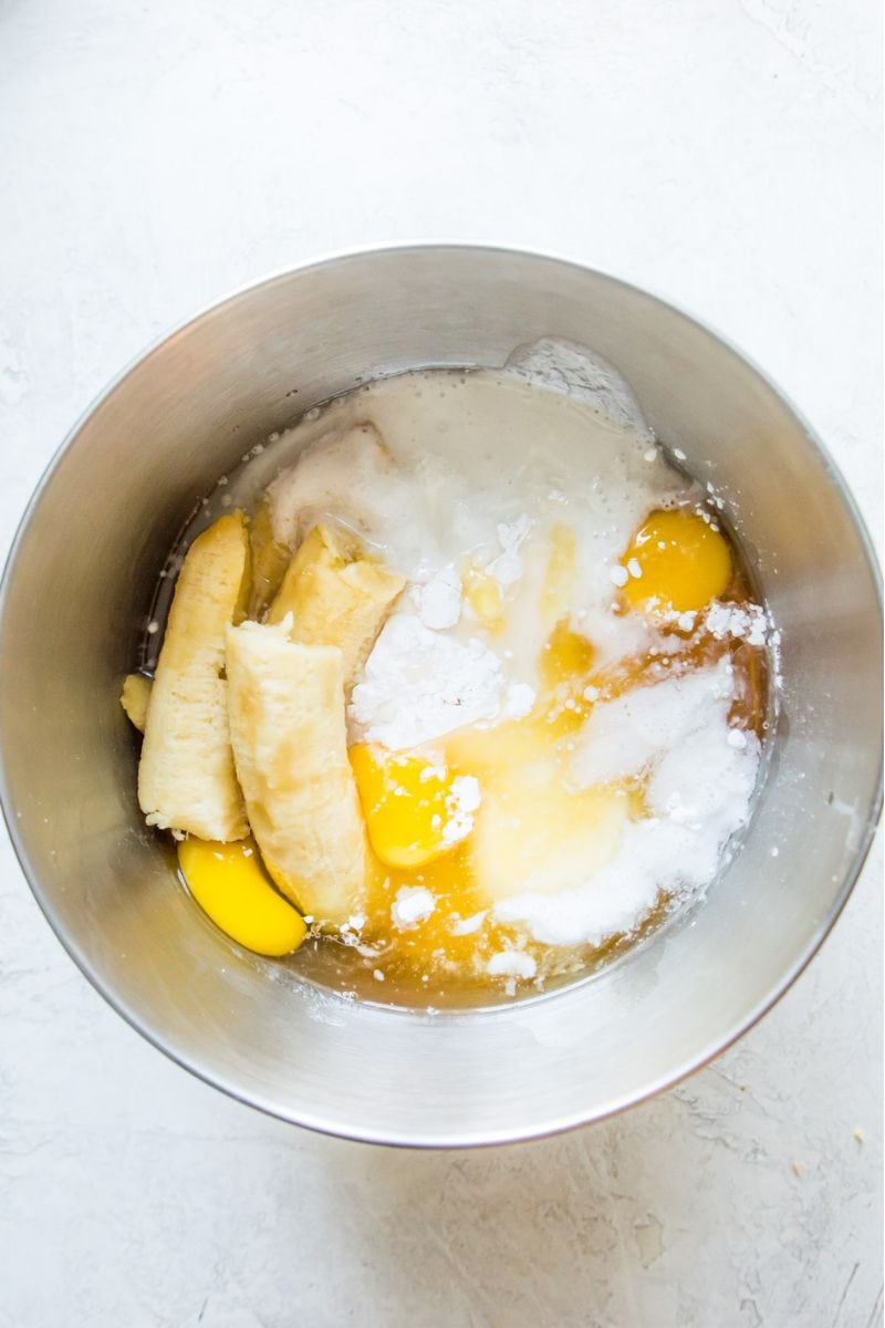A mixing bowl filled with bananas, eggs, flour and honey.