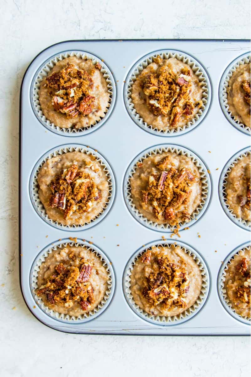 A muffin tray filled with muffin batter and topped with pecan pieces.