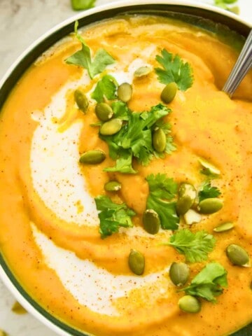 A bowl of pumpkin and sweet potato soup topped with chopped cilantro and pumpkin seeds.