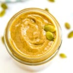 A jar of pumpkin seed butter garnished with a couple pumpkin seeds.