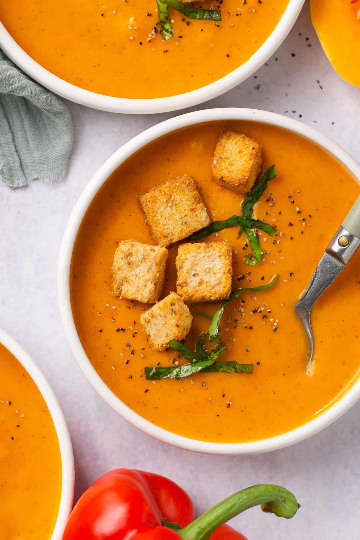 Bowls of squash and red pepper soup topped with croutons and black pepper. 