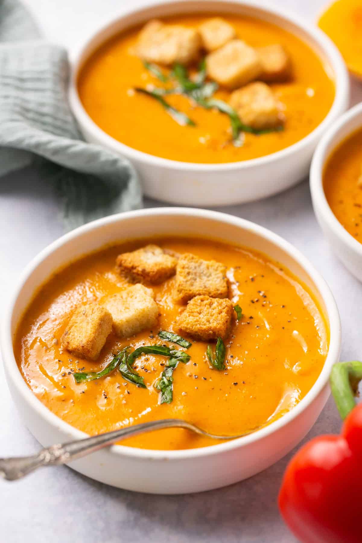Bowls of roasted red pepper and butternut squash soup topped with croutons and fresh herbs. 