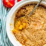 A white casserole dish filled with a turnip and apple casserole with a serving spoon in it.