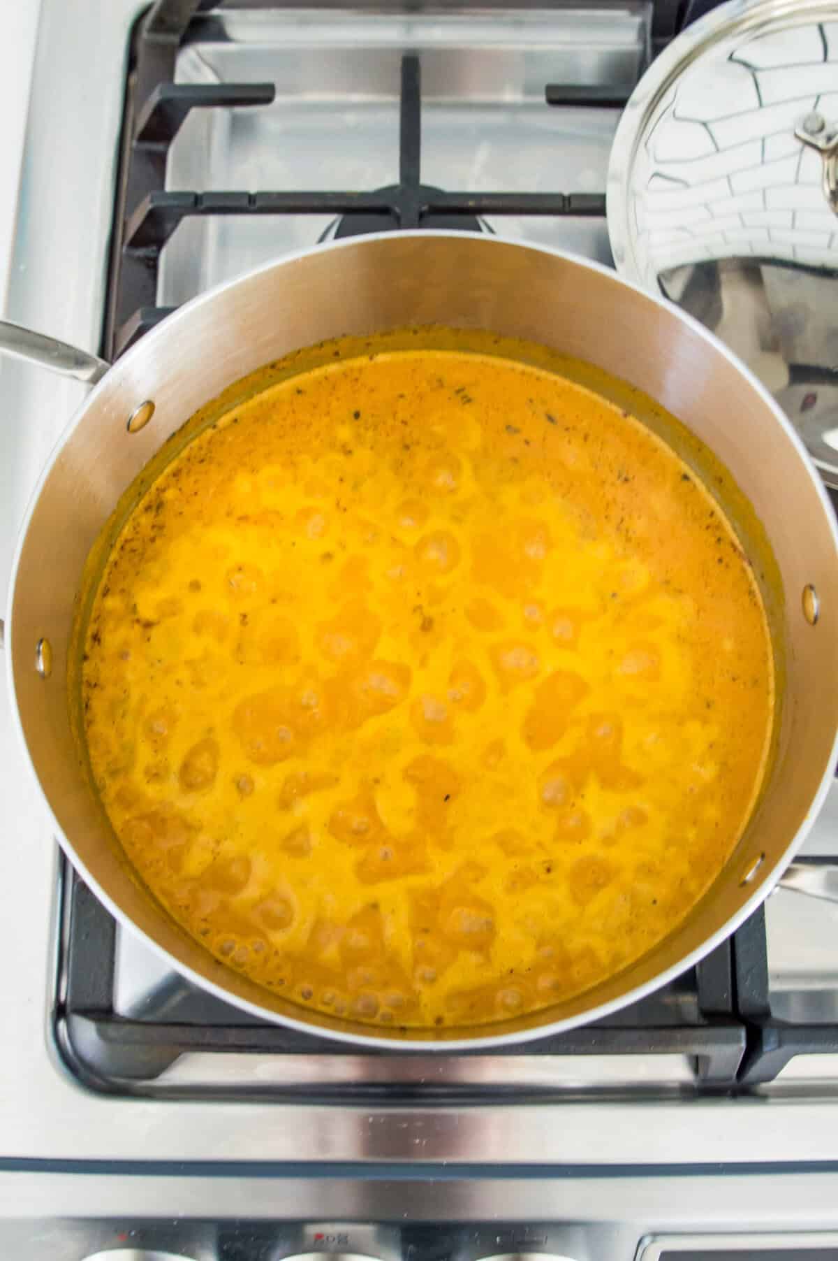 A pot on the stovetop with an orange liquid simmering in it.