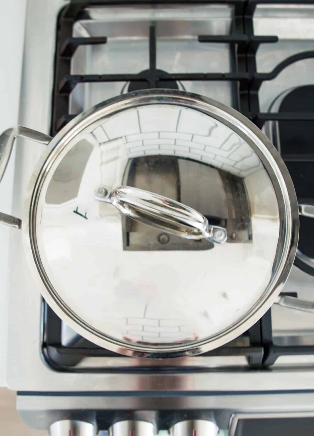 A pot on a stovetop with a lid on the pot.