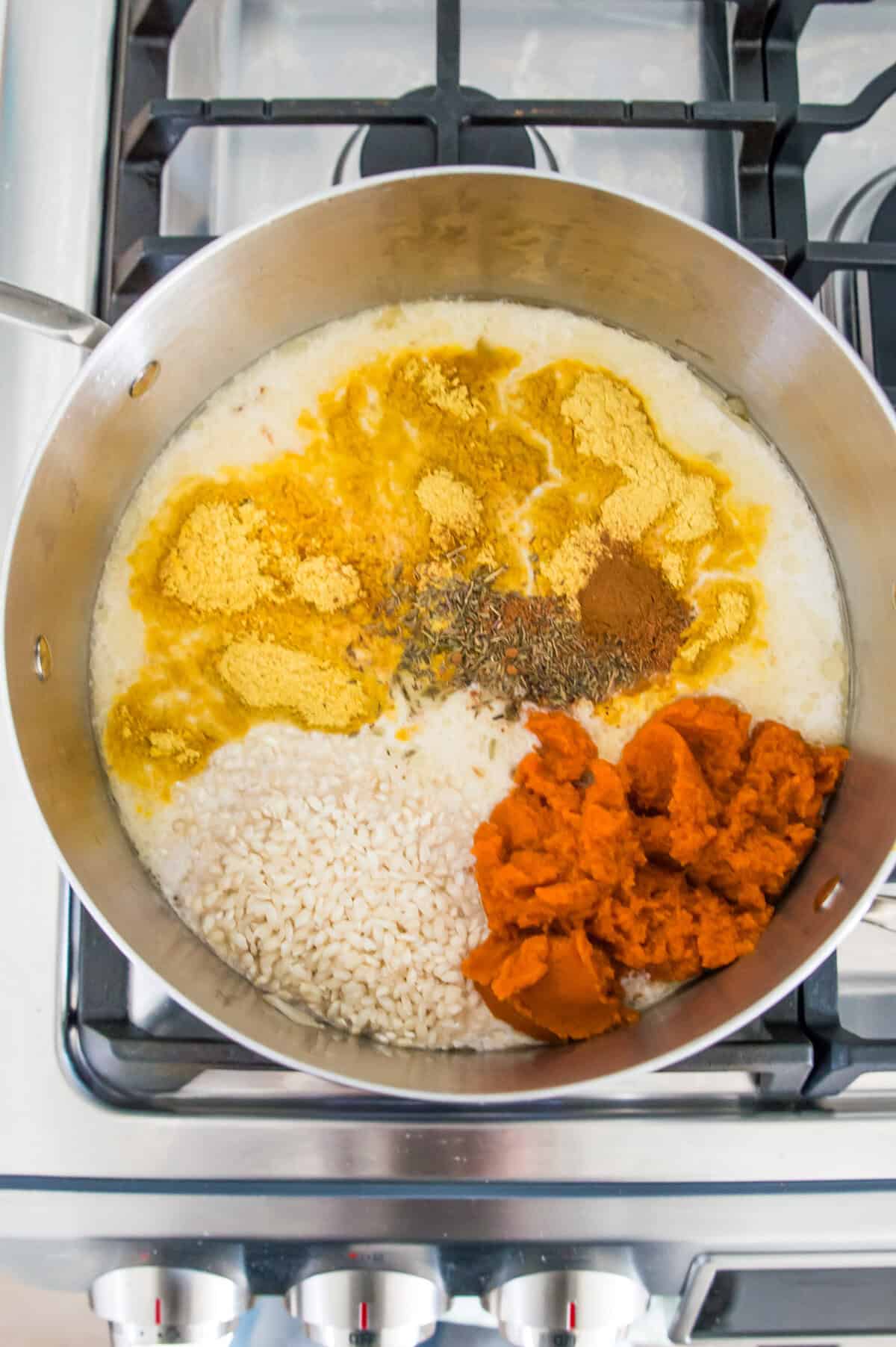 A pot on the stovetop with coconut milk, white rice, pumpkin puree and nutritional yeast in it.