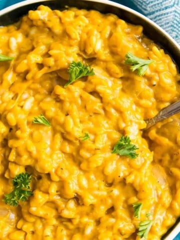 A bowl of vegan pumpkin risotto with a spoon in it and garnished with fresh parsley.