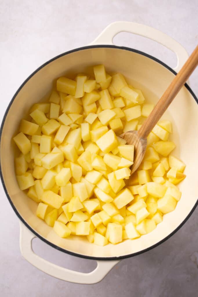 A pot with apple pieces cooking in it and a spoon in the pot.