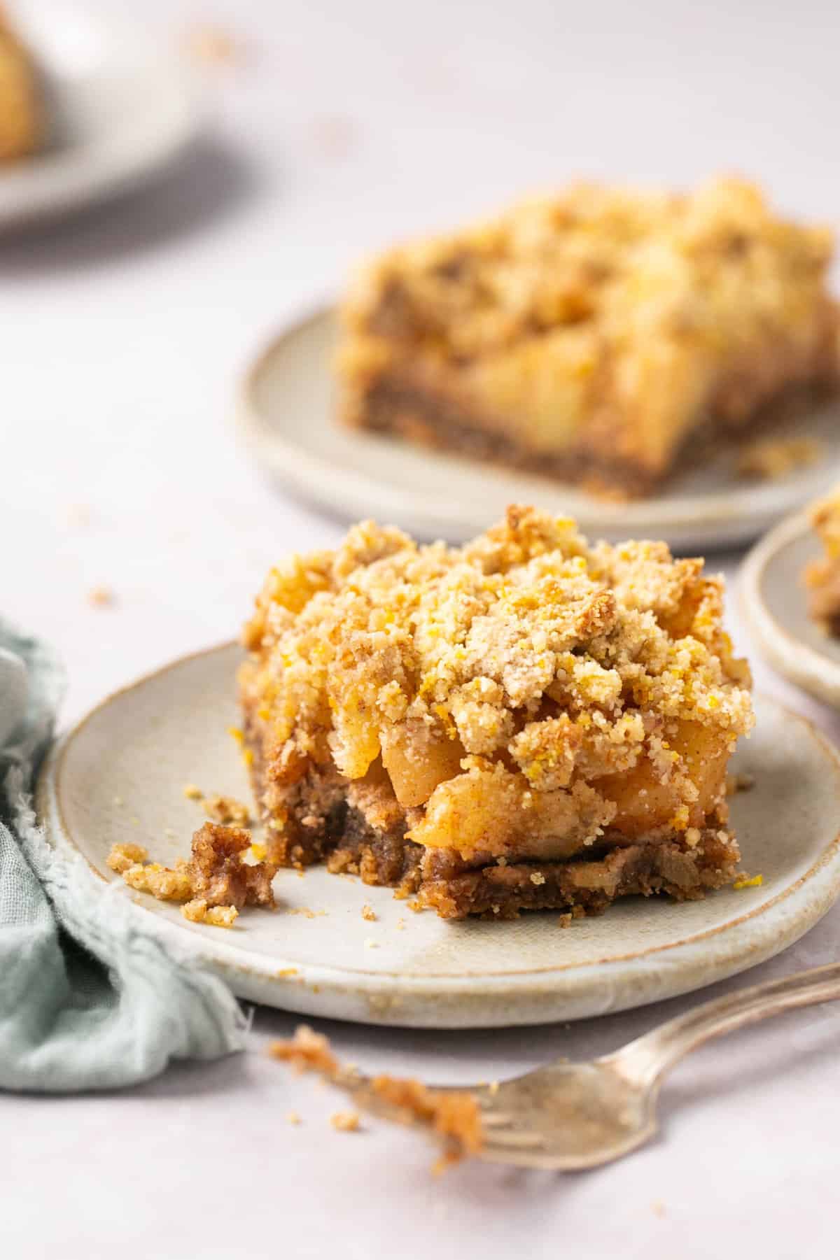An apple crumble bar on a plate with a bite out of it.
