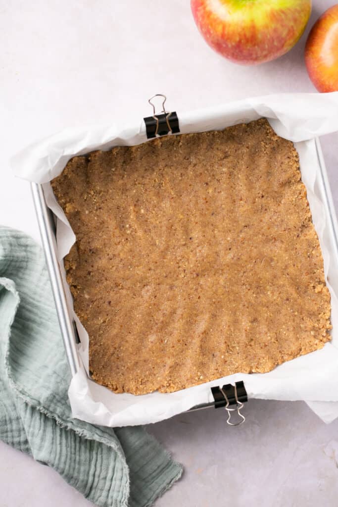 A square baking pan lined with parchment paper with a crust in it.