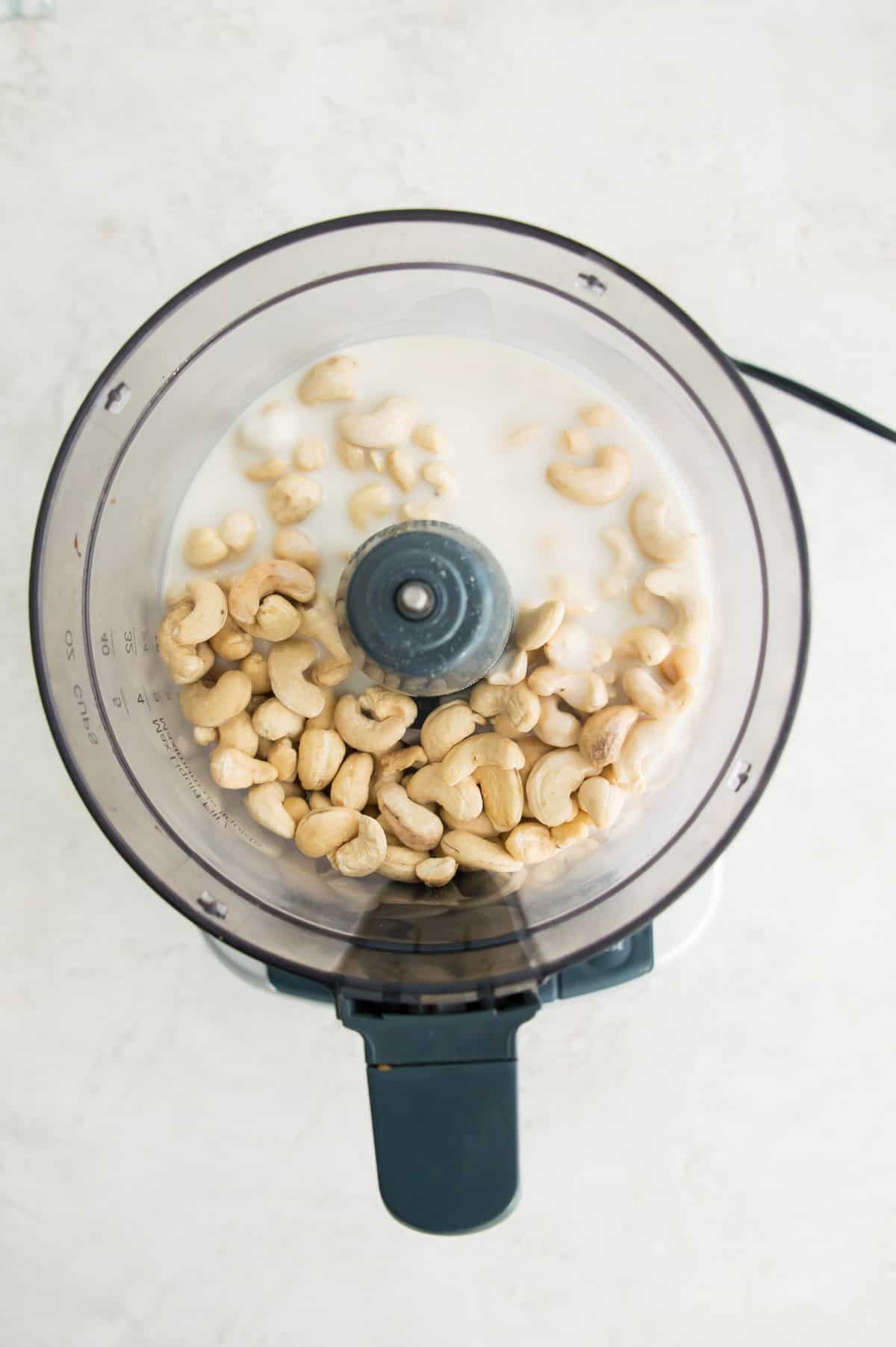 A food processor with raw cashews and melted coconut butter in it.
