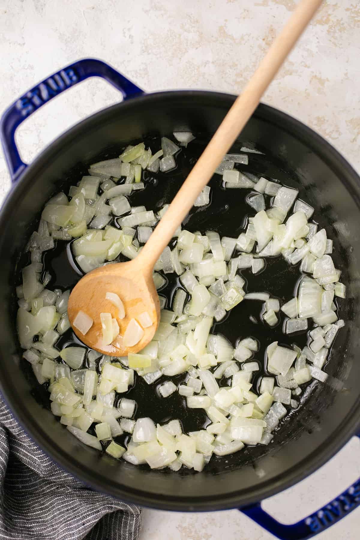 A pot with chopped onions being cooked in it and a wooden spoon in the pot with the onion. 