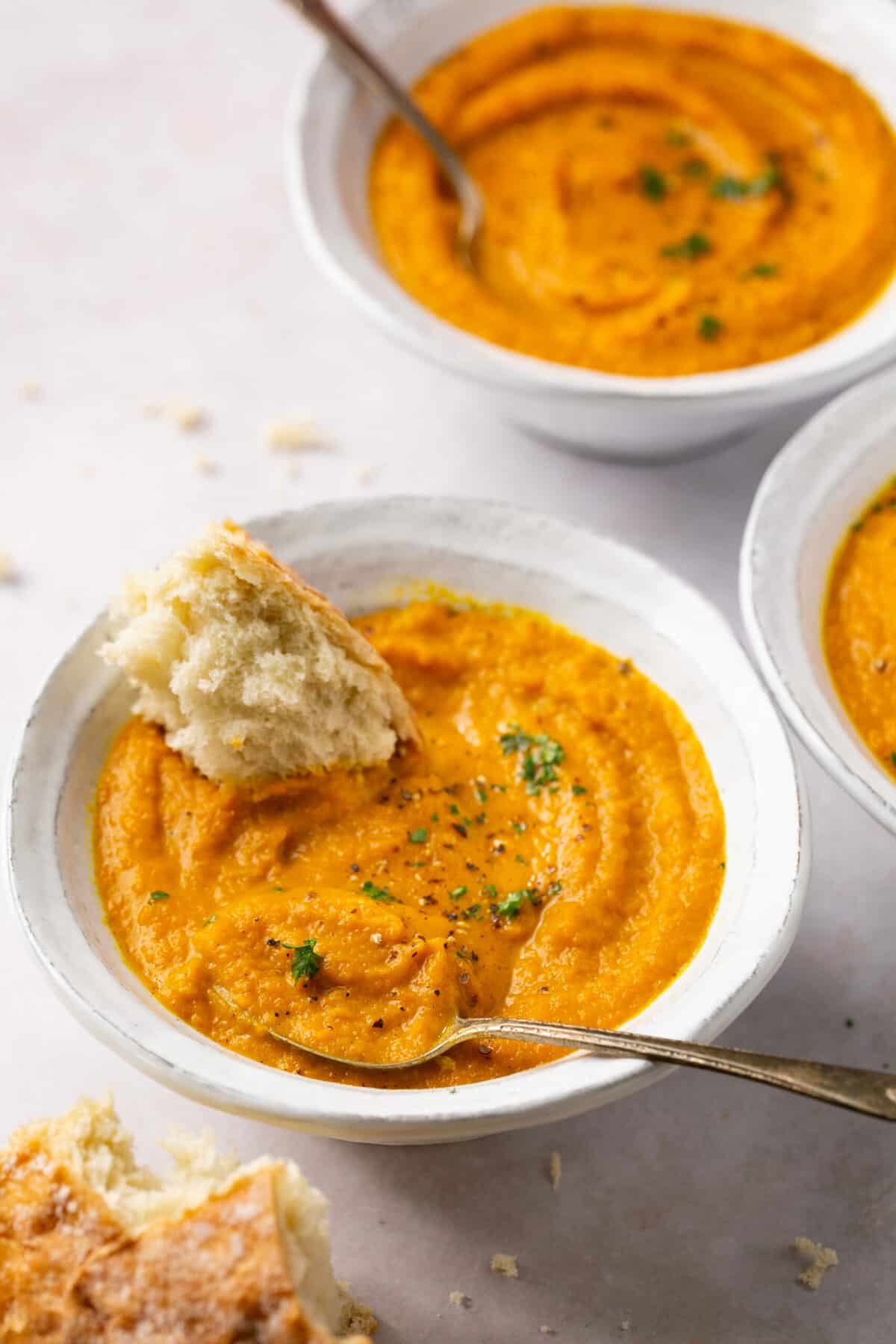 Bowls of creamy carrot turnip soup, with a piece of crusty bread in it.