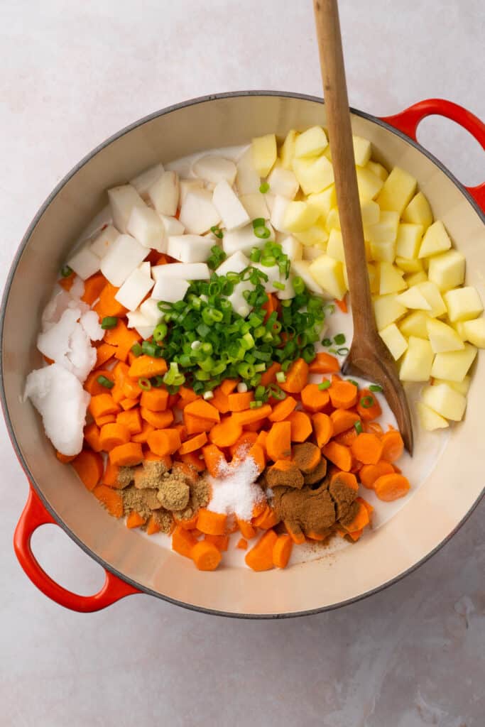 A pot filled with chopped carrots, turnips, onion, coconut milk and spices.
