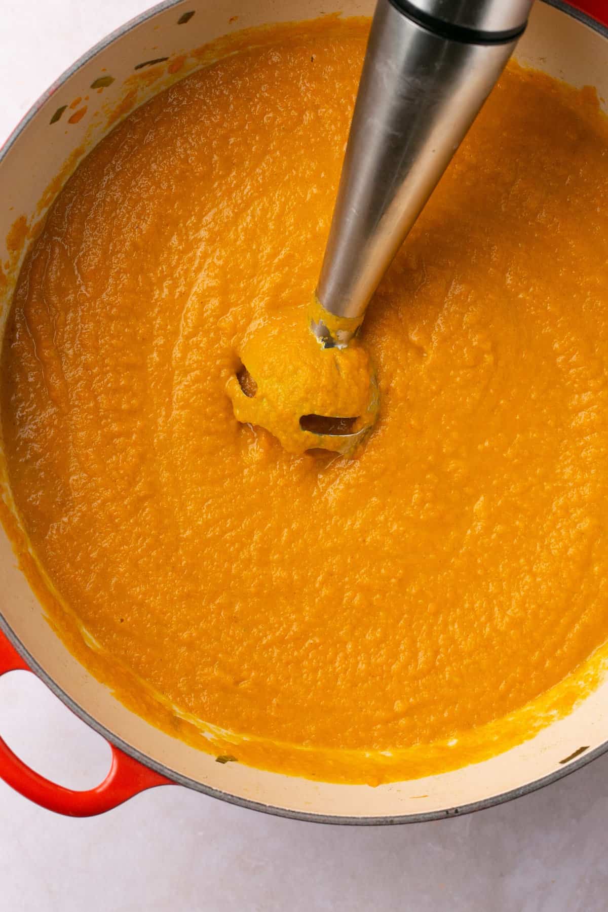 A pot filled with a creamy carrot soup with an immersion blender in it.